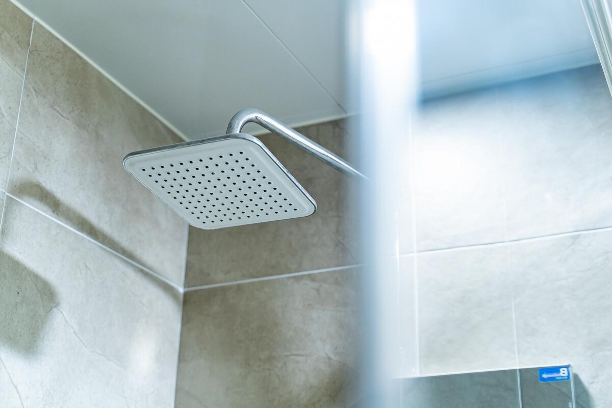 A showerhead with a square design and multiple holes, mounted on a wall with a tiled surface.