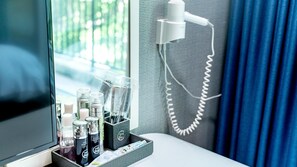 Hotellihuone, jossa on erillinen alue meikkausta ja hiustenhoitoa varten. Tällä alueella on peili, hiustenhoitotuotteita ja hiustenkuivaaja, joka on sijoitettu jalustalle.