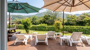 An outdoor deck with white plastic chairs and tables, a wooden picnic table, and two large umbrellas providing shade. - Namwon Hanjeungwonstay Pension (Namwon)