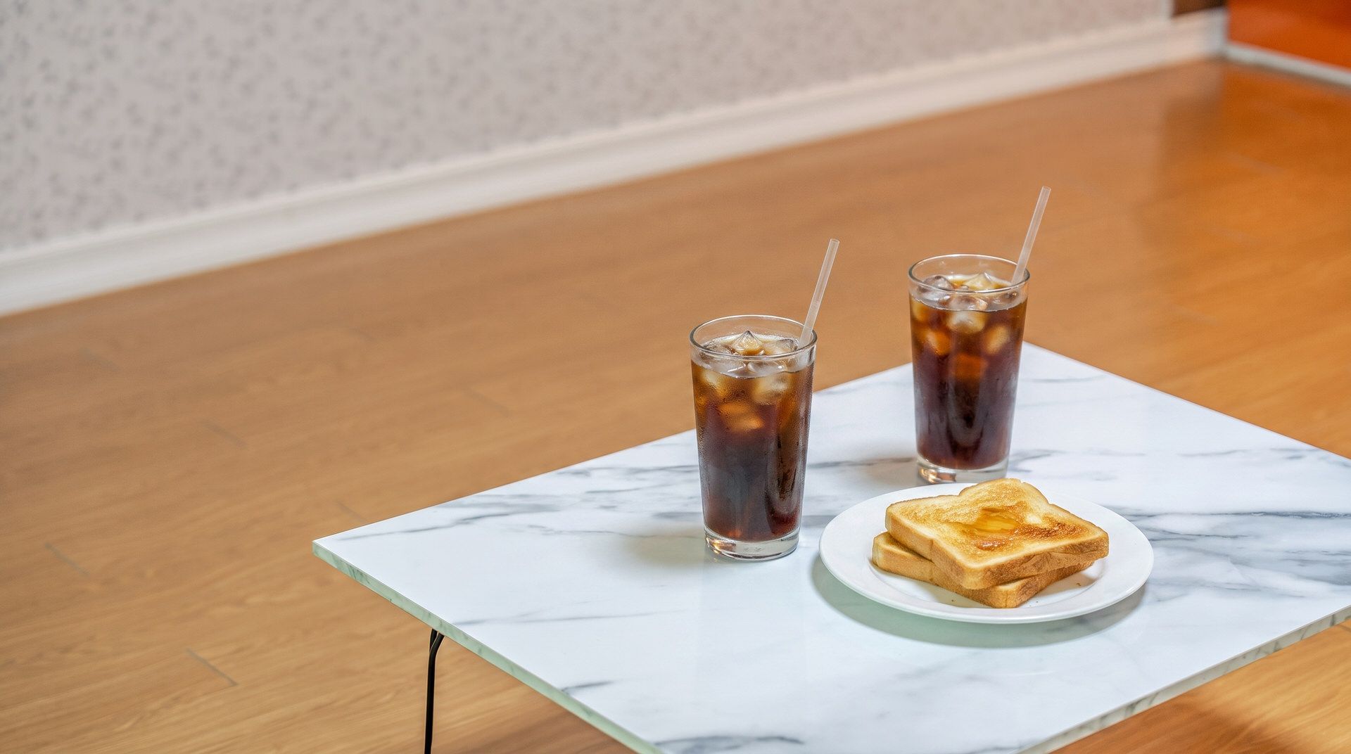 Una mesa de mármol con dos vasos de té helado y una rebanada de tostada.