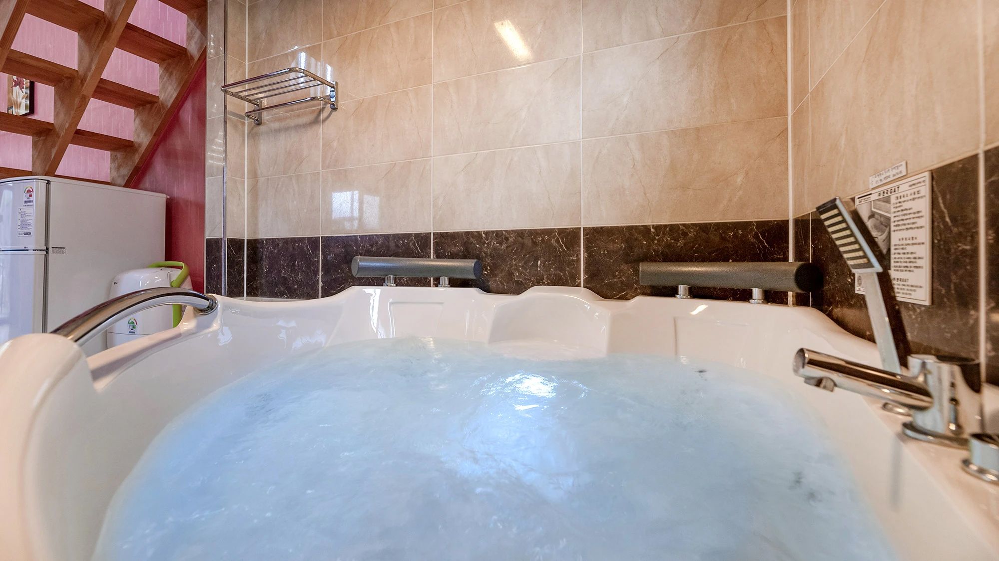 A bathroom with a bathtub filled with water, a towel rack, a shower head, and a toilet.