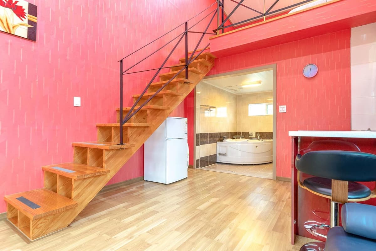 A modern apartment with a wooden staircase, a kitchen with a sink and a refrigerator, and a bathroom with a bathtub.