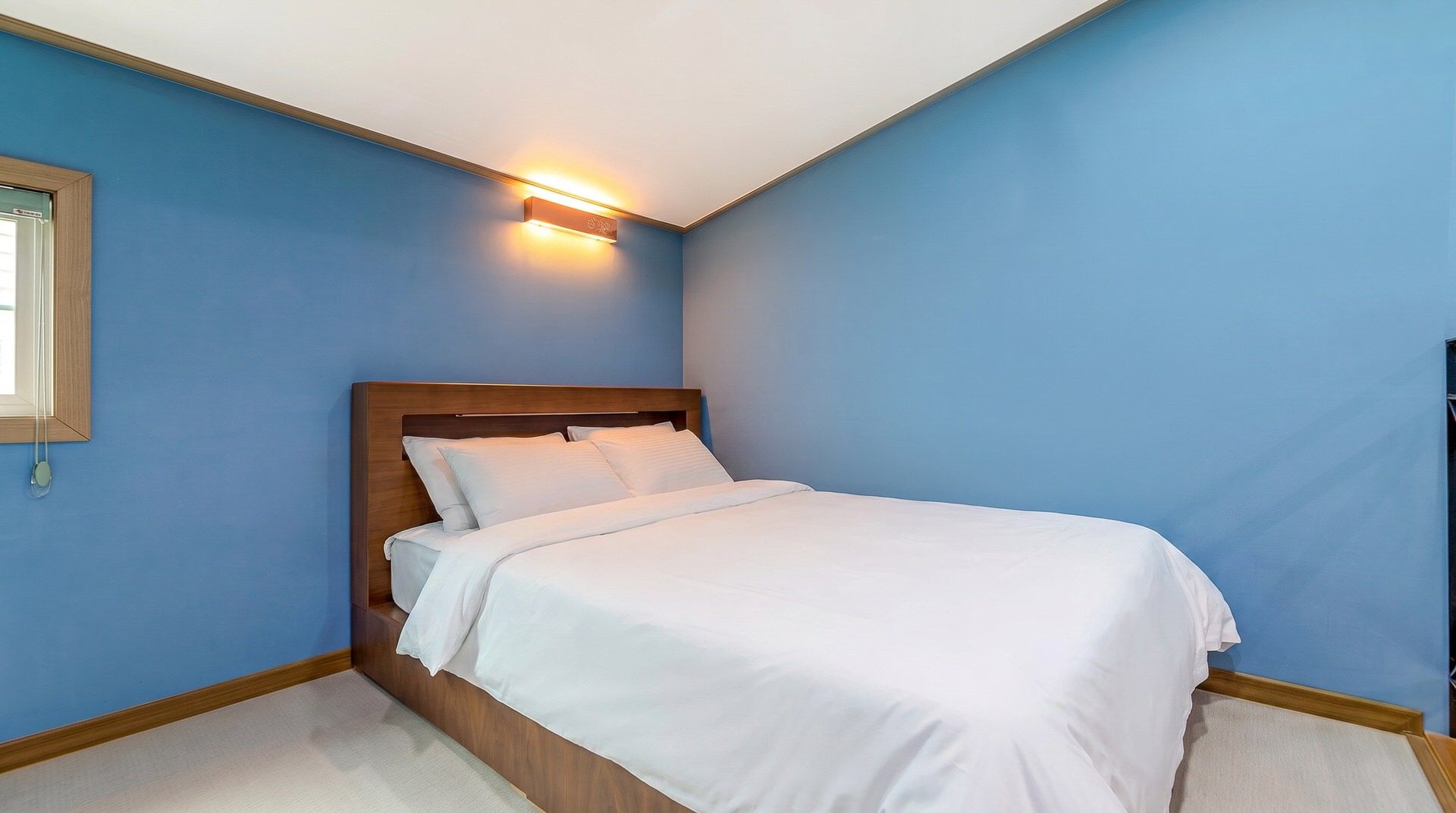 A bedroom with a single bed, a nightstand, and a wall-mounted light fixture.