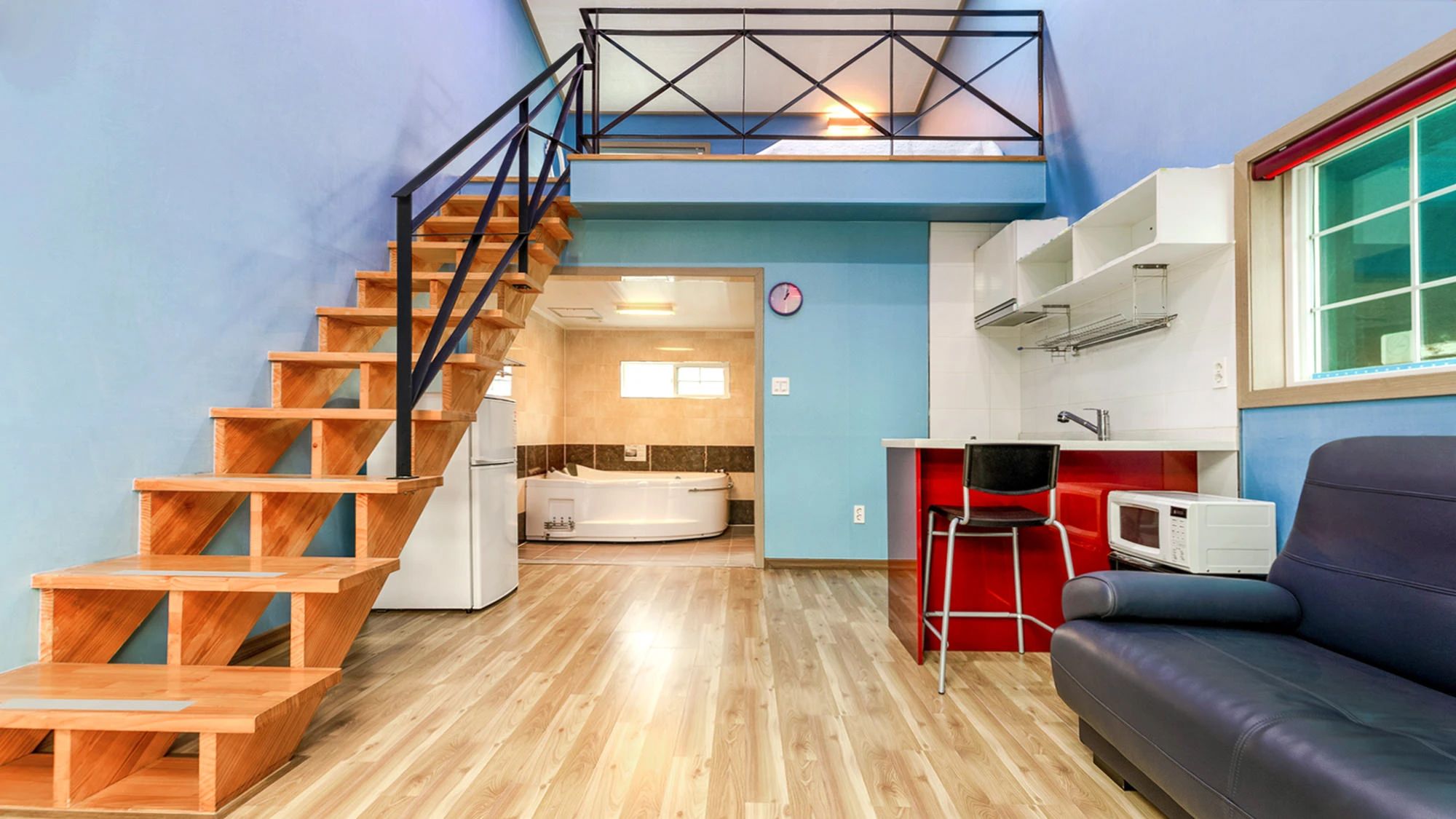 A compact living space with a wooden staircase, a kitchenette, a seating area, and a bathroom.