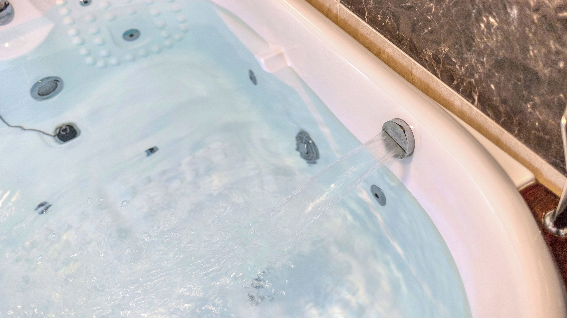 A hot tub with water flowing from a faucet, surrounded by a tiled area.