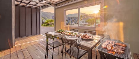 Un espacio de comedor al aire libre con una parrilla, piso de madera y vistas del paisaje.