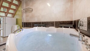 A bathroom with a large bathtub, a towel rack, and a refrigerator.
