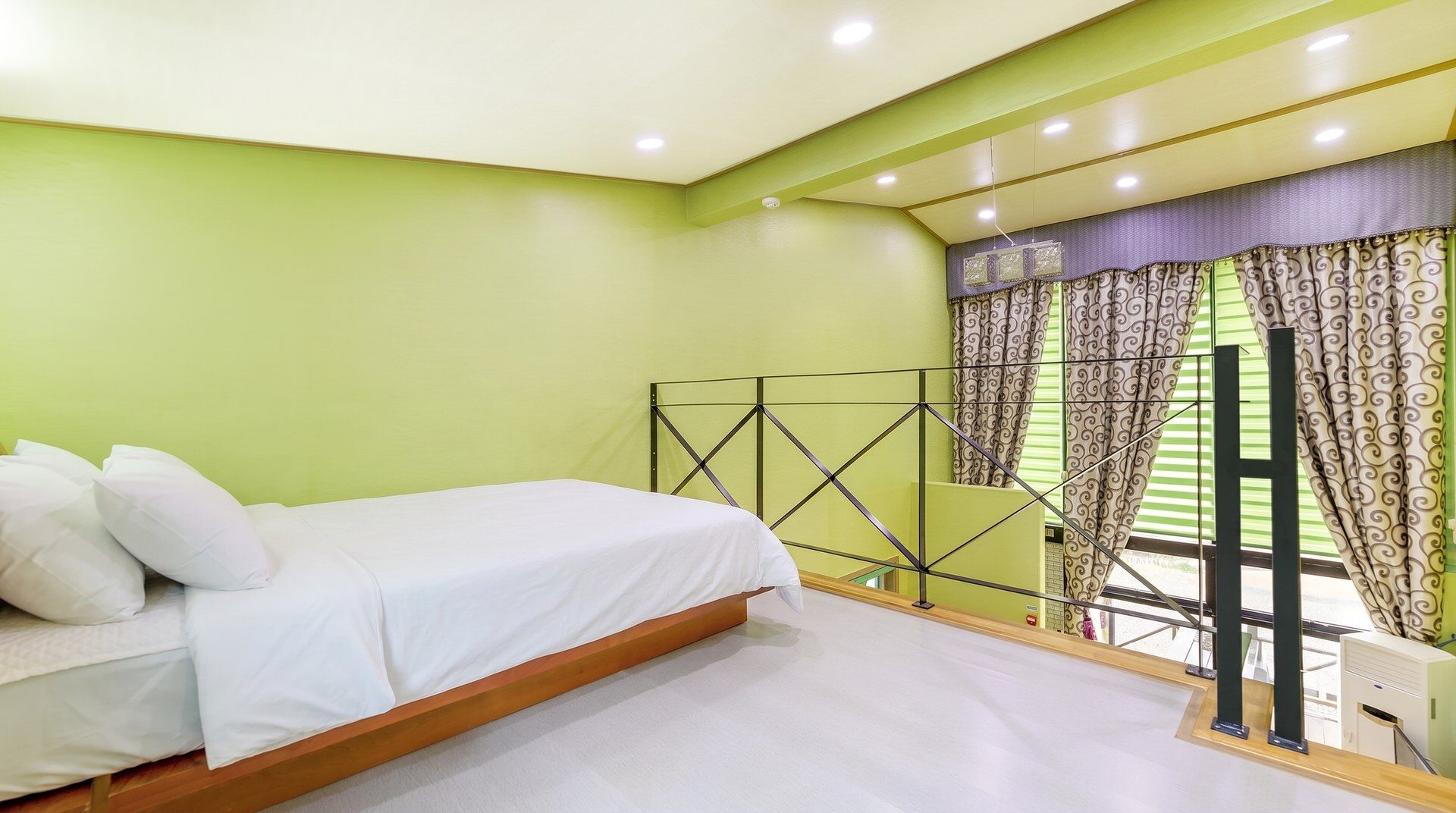 A bedroom with a bed, a window with curtains, and a balcony with a railing.