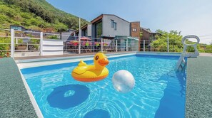 En swimmingpool med en badanka och en boll, omgiven av ett staket och hus i bakgrunden.