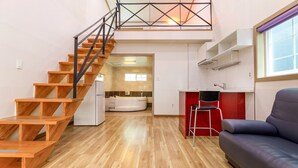 Un appartement moderne doté d’un escalier en bois, d’une cuisine avec un mur d’accent rouge et d’un salon avec un canapé.