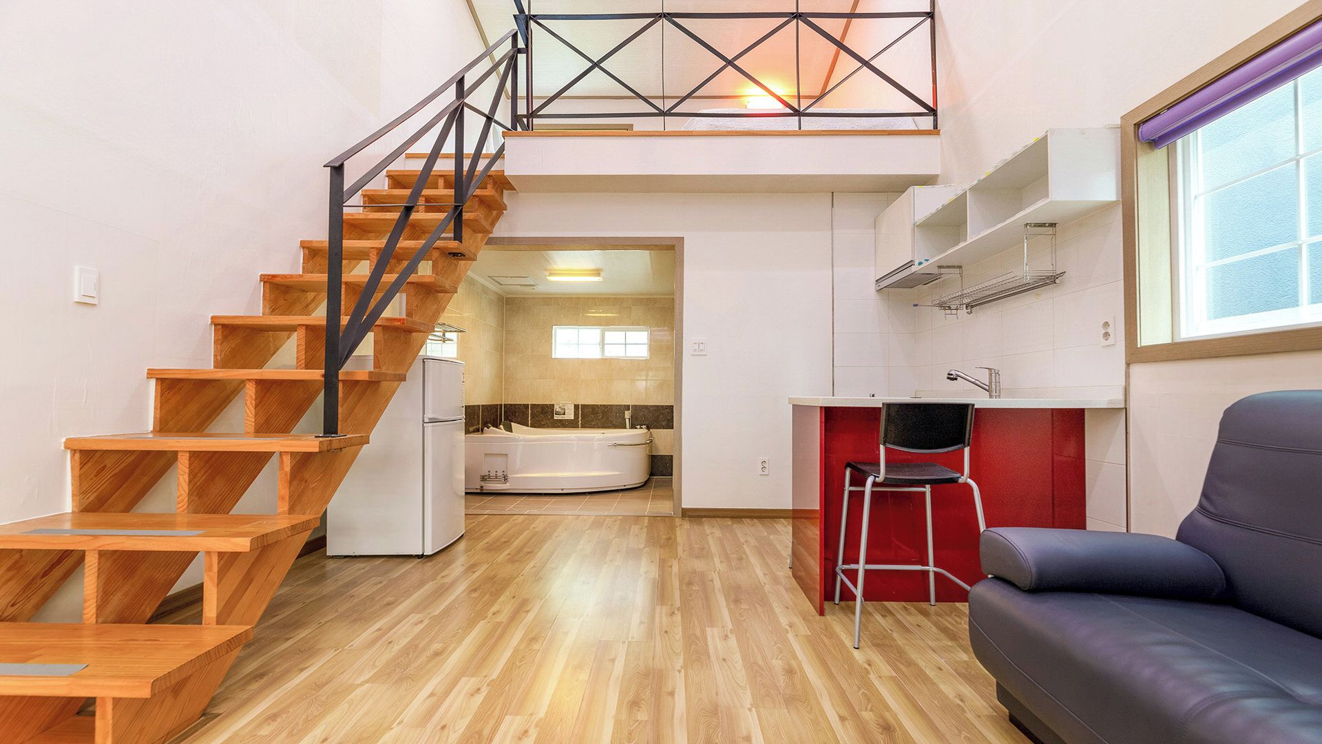 A modern apartment with a wooden staircase, a kitchen with a red accent wall, and a living area with a sofa.