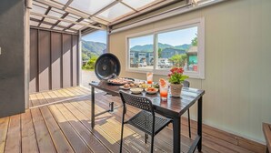 Une terrasse avec un barbecue, une table, des chaises et une vue sur les montagnes.