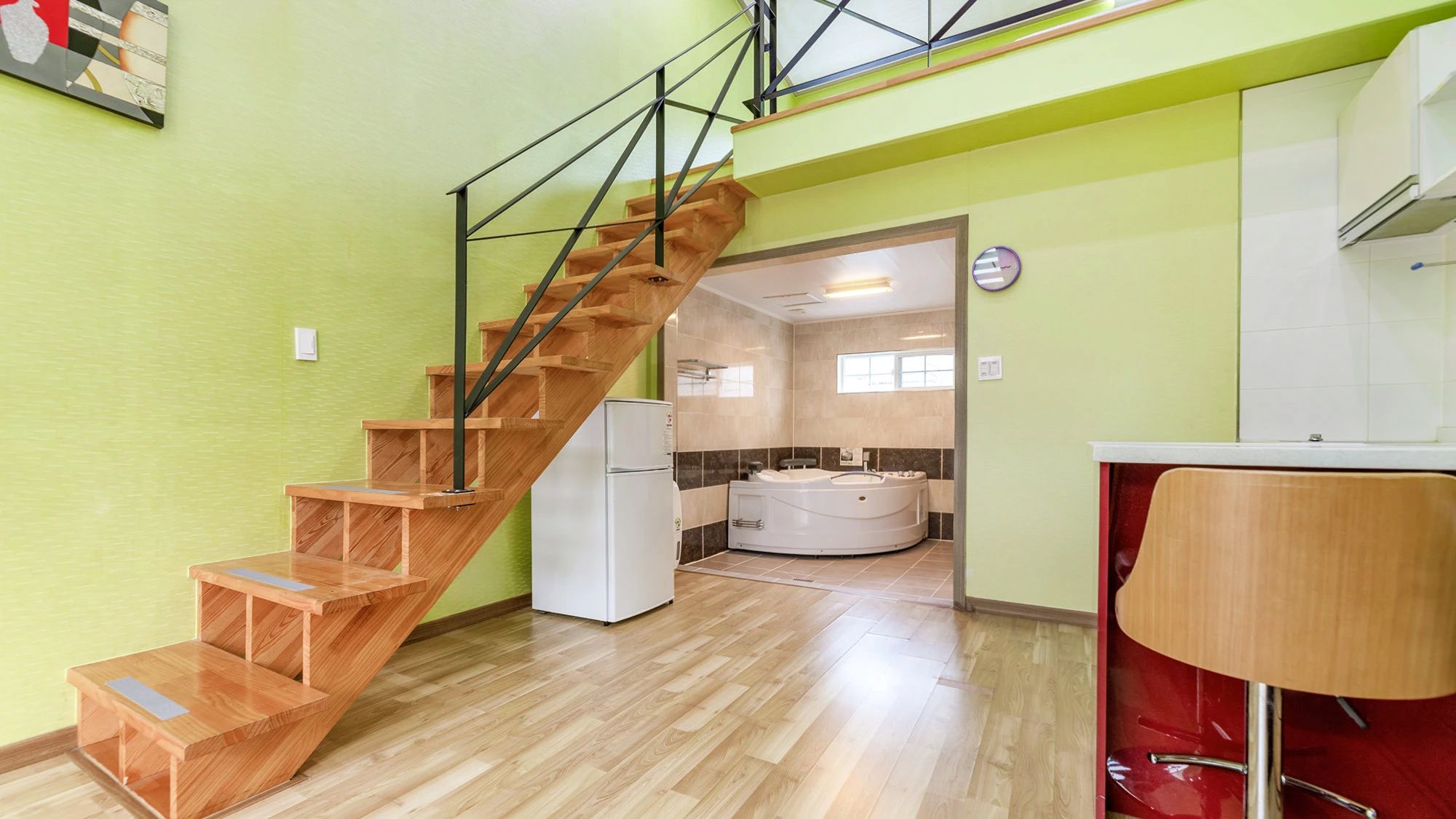 A modern interior with a wooden staircase, a kitchen area, and a bathroom with a bathtub.