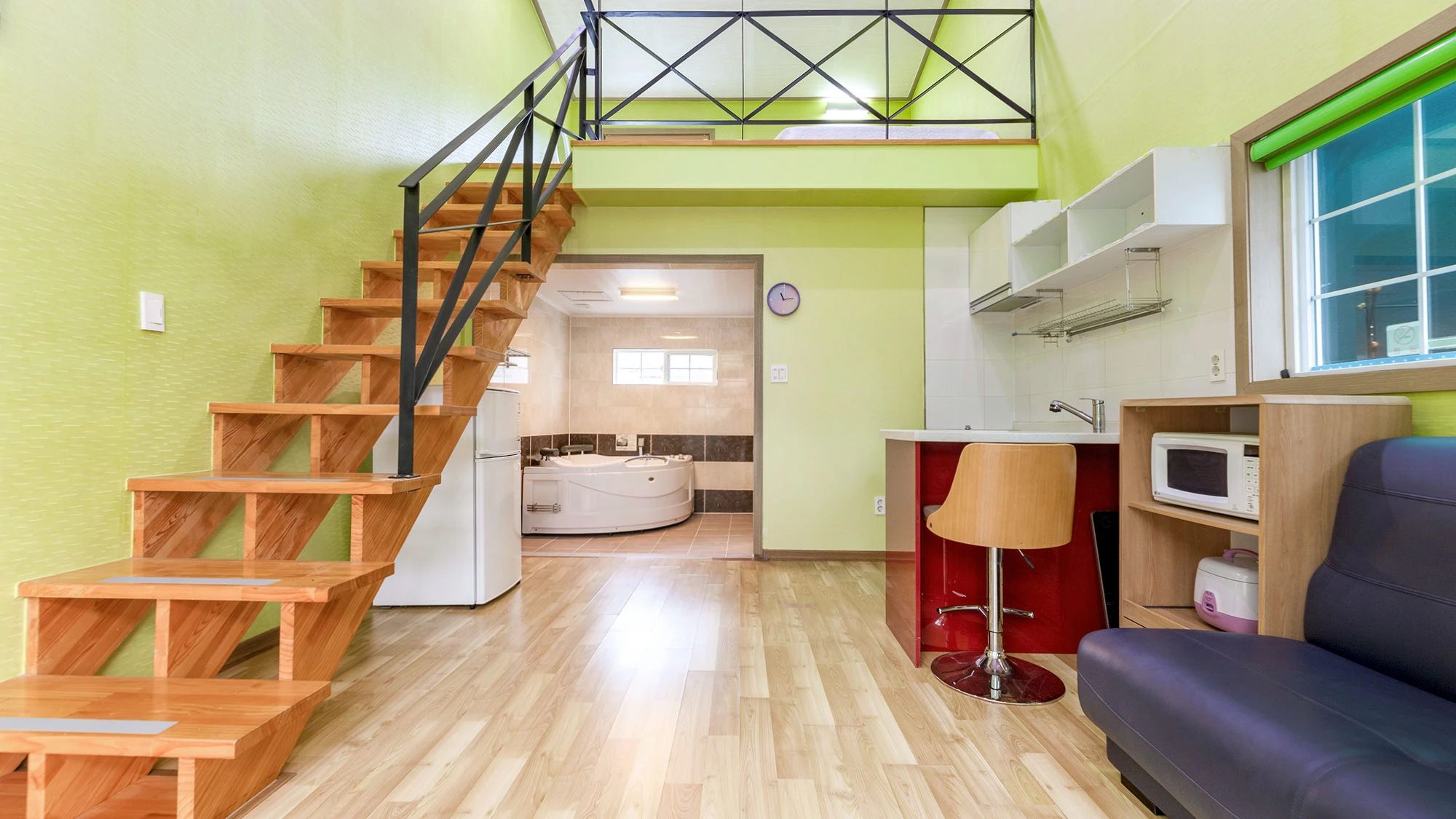 A staircase leading to a second floor, a kitchen area with a microwave, a red chair, and a sofa.