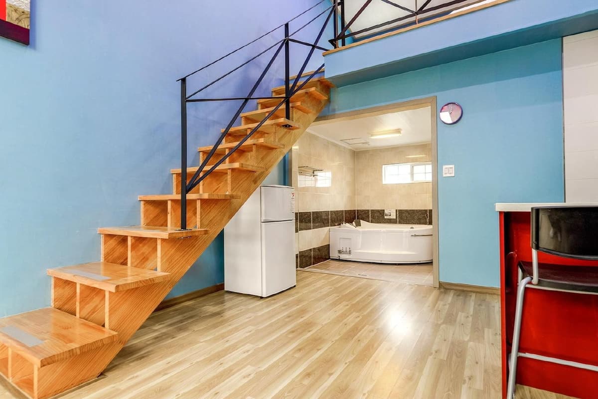 A compact apartment with a wooden staircase, a kitchen with a modern design, and a red chair.