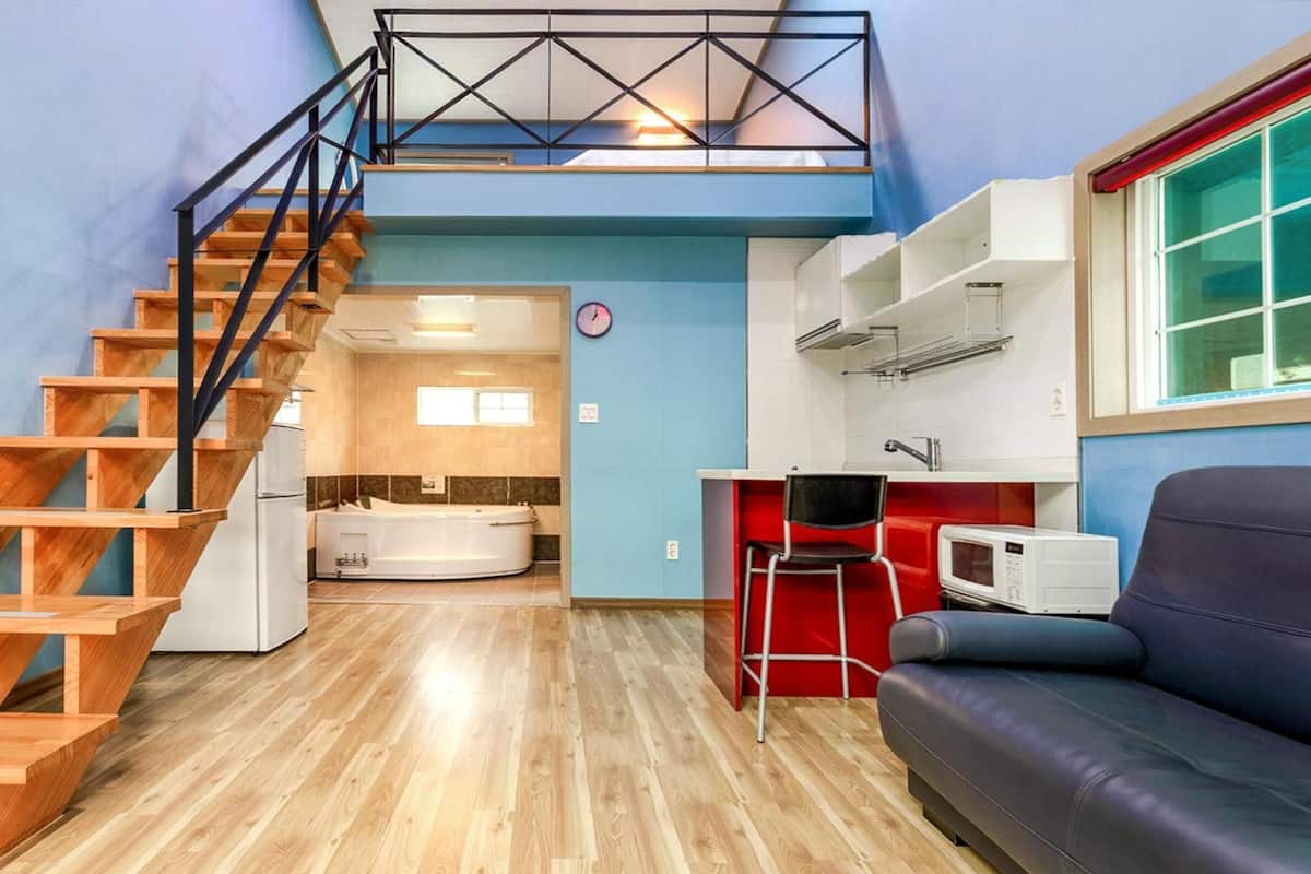 A compact living space with a wooden staircase, a kitchen area, a seating area, and a visible bathroom.