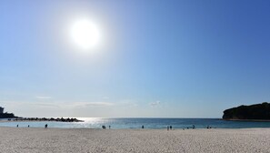 Ein Strand mit blauem Himmel und ruhigem Wasser, mit sandigem Ufer und einem Felsen im Hintergrund.