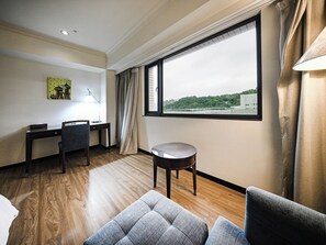 A hotel room with a wooden floor, a desk with a chair, a round table, a sofa, and a large window with a view of buildings and greenery. - CHECK inn Taipei Neihu (Taipei)