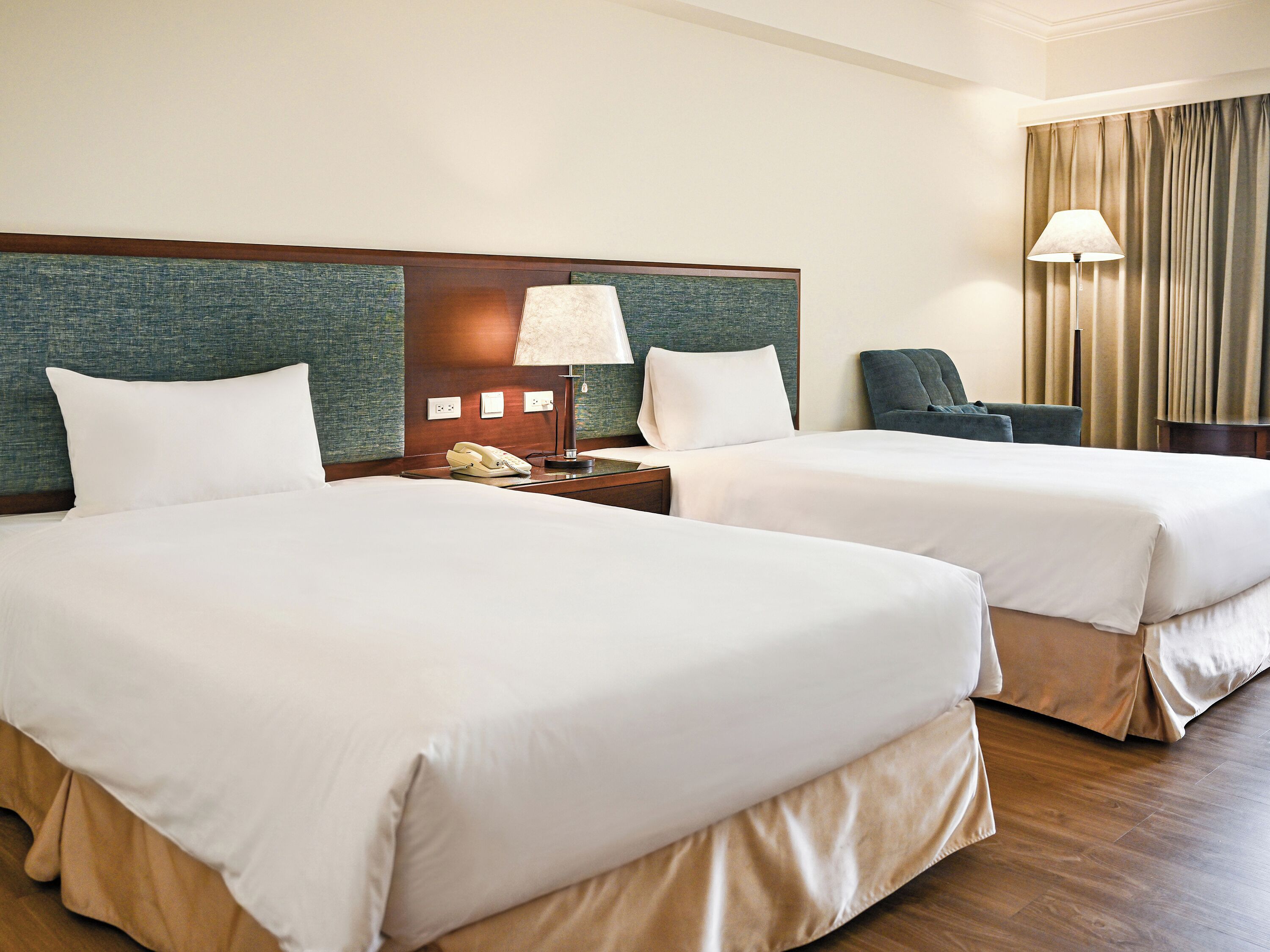 Een hotelkamer met twee bedden, een nachtkastje met een lamp, een telefoon en een stoel.