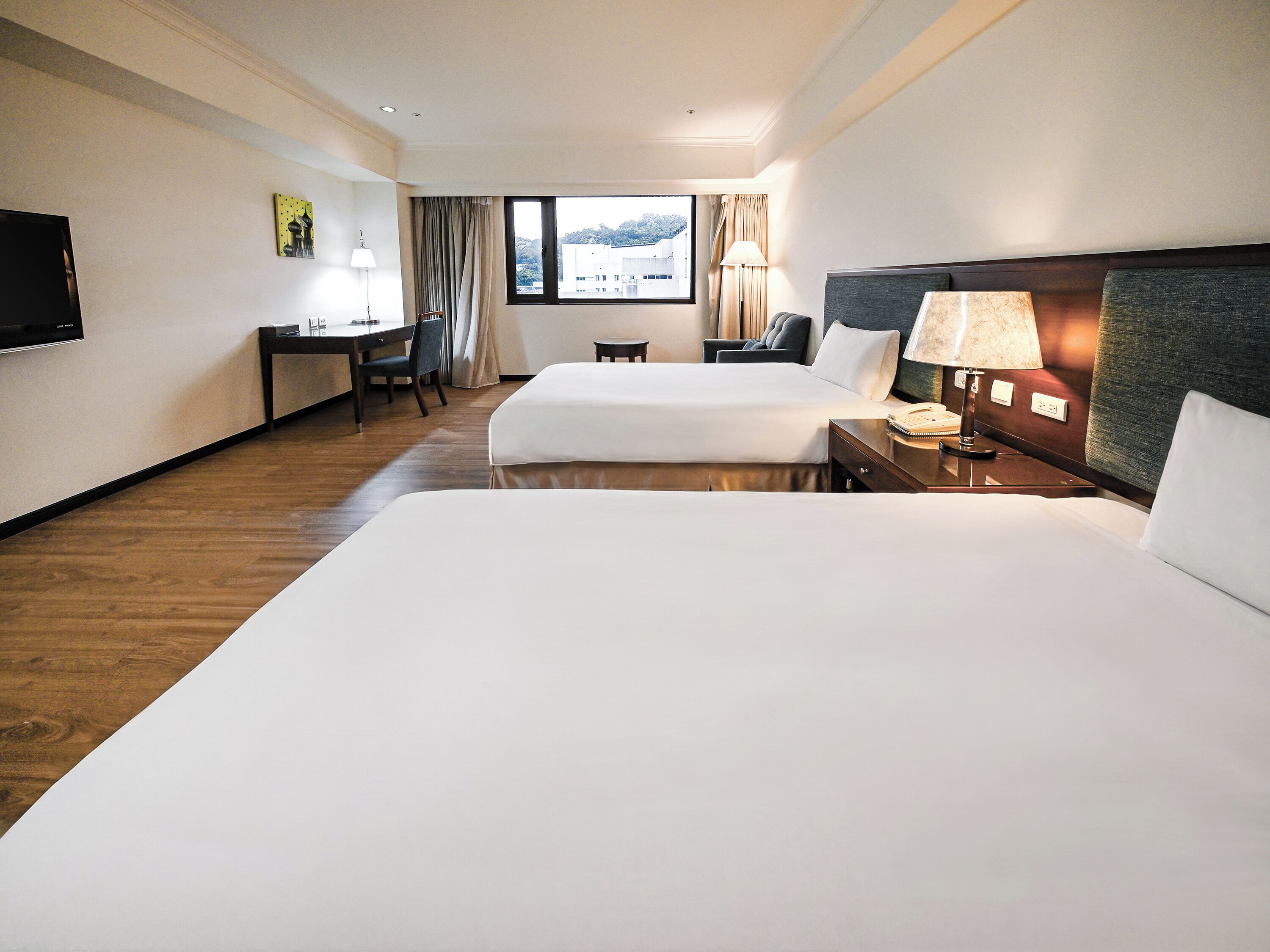 A hotel room with two beds, a desk, a chair, a TV, and a window with a view.
