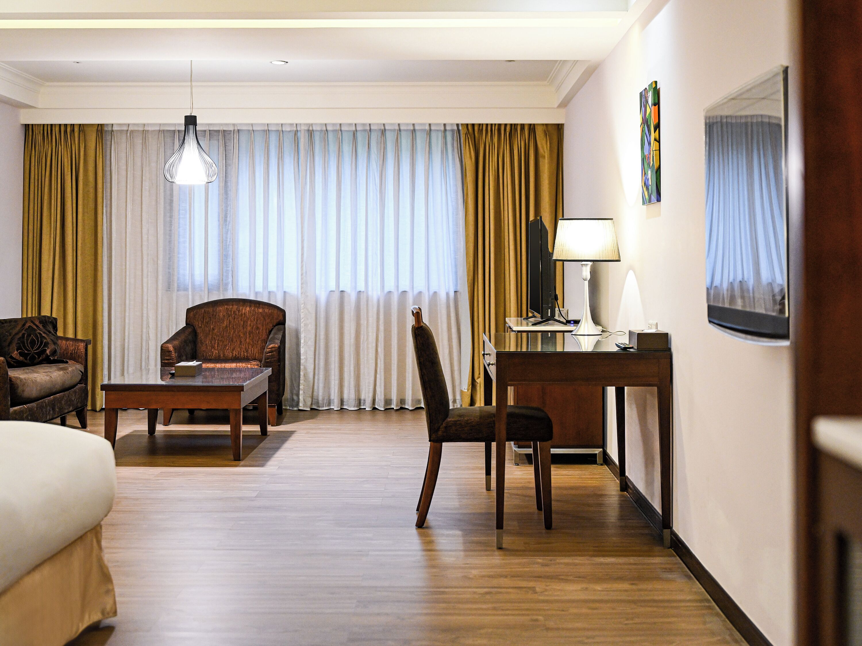 A hotel room with a bed, a desk, a chair, a lamp, a television, and curtains.