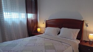 Una cama bien hecha con colcha, dos lámparas de noche y un cabecero de madera.