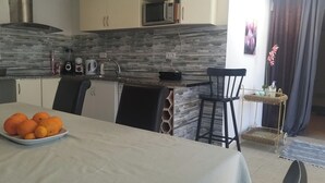 Una cocina moderna con salpicadero de piedra, microondas y un lavabo. Hay una mesa de comedor con un plato de naranjas.