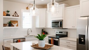 Een moderne keuken met witte kasten, roestvrijstalen apparatuur en hanglampen.