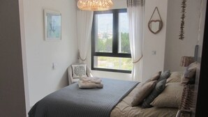 Un dormitorio con cama, una silla, una ventana y una lámpara colgante.