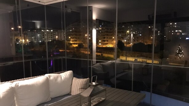 Una sala de estar moderna con un ventanal grande, un sofá y una pequeña mesa con una lámpara.