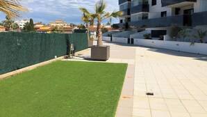 Un edificio moderno de apartamentos con balcones, un césped verde y un seto.