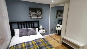 A modern bedroom with a bed, bedside tables, a mirror, and artwork on the wall. - Lovely 2-Bed Apartment in Coventry (Coventry)