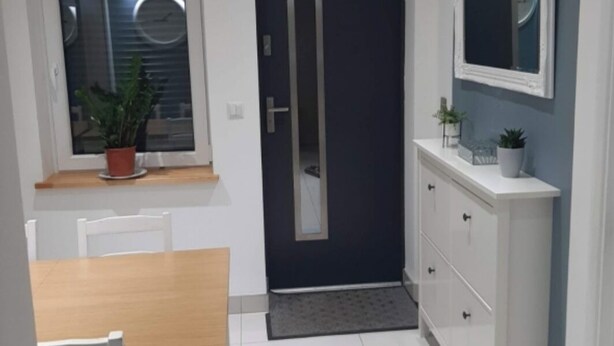 A modern kitchen with a dining area, a dark door, and a white cabinet with a mirror. - Lovely 2-Bed Apartment in Coventry (Coventry)