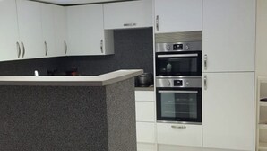 A modern kitchen with a central island, built-in ovens, and a dark backsplash. - Lovely 2-Bed Apartment in Coventry (Coventry)