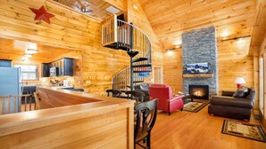A log cabin interior with a spiral staircase, a stone fireplace, a dining area, and a living room with a sofa and a red chair. - Cozy 2bedroom cabin near Island / Dollywood at Pigeon Forge  with Panormic Views (Sevierville)