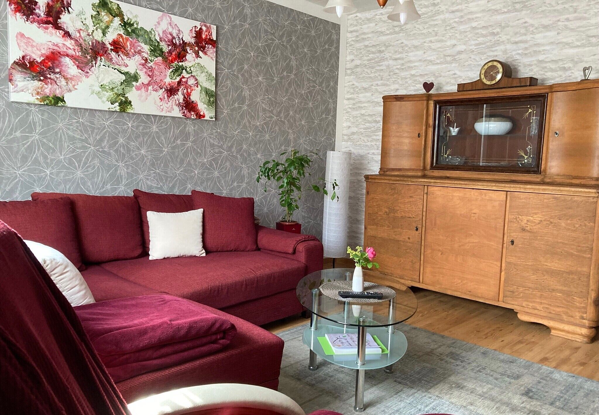 A living room with a red sofa, a glass coffee table, a wooden cabinet, and a floral painting on the wall.