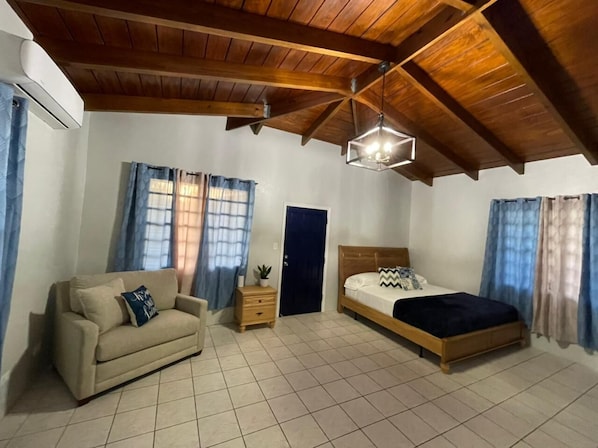 Quarto com teto de madeira, uma cama, um sofá e uma mesa de cabeceira.