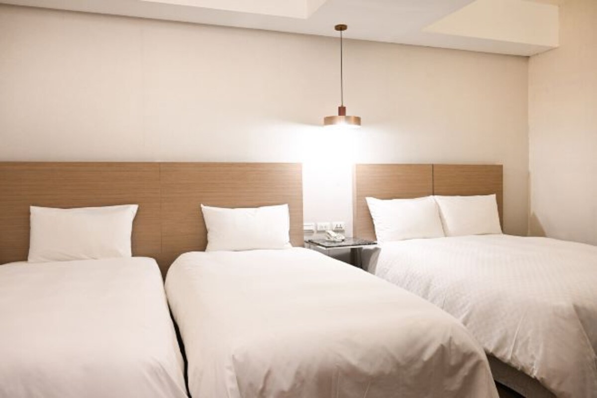 A hotel room with two beds, a wooden headboard, a nightstand, and a hanging light fixture.