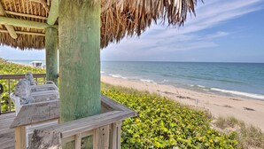 Eine Holzterrasse mit einem Reetdach mit Blick auf einen Strand.