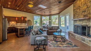 A spacious living area with a stone fireplace, a kitchen with wooden cabinets, and a large window overlooking a garden.