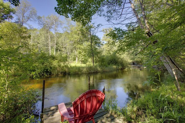 Une jetée en bois avec une chaise rouge qui s’avance sur une rivière paisible, le tout entouré d’une forêt dense.