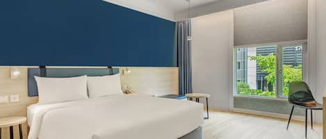 Habitación de hotel moderna con una cama grande, mesitas de noche, una silla y vistas al verdor por la ventana.