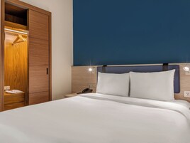 A hotel room with a bed, a bedside phone, a nightstand, and a wardrobe.