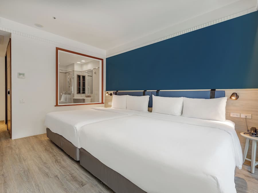 Quarto de hotel com cama grande, espelho, mesa de cabeceira com luminária e vista para o banheiro.
