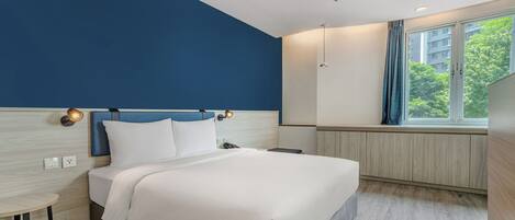 Una habitación de hotel moderna con una cama, mesita de noche y ventana con vistas a zonas verdes.