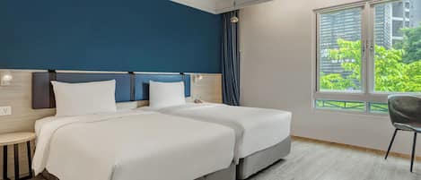 A hotel room with two beds, a nightstand, a chair, a window with a view of greenery, and a ceiling light.