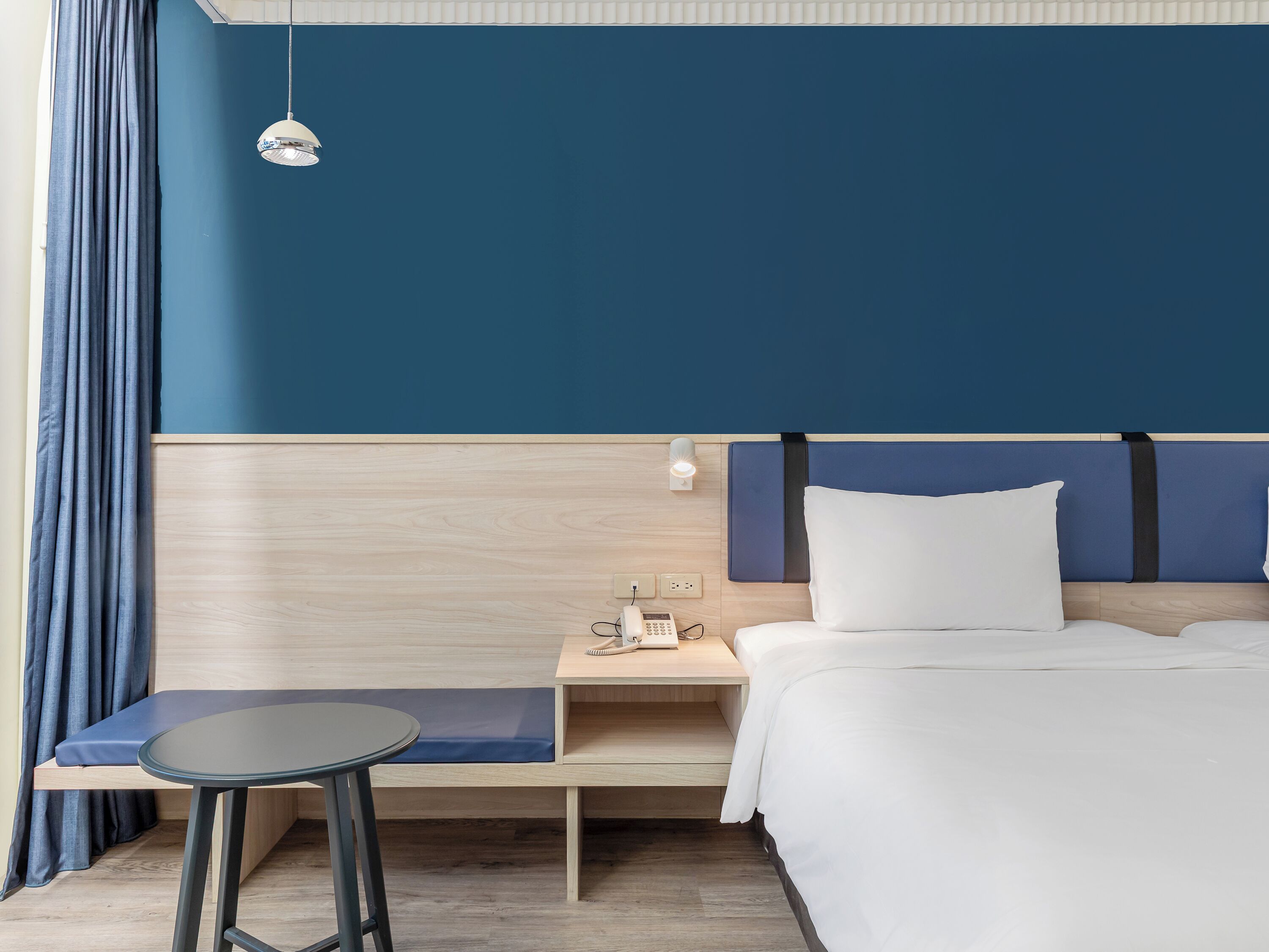 Et hotelværelse med seng, sengebord, lampe og bænk.