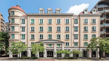 Een hotel met meerdere verdiepingen, een klassiek gevelontwerp, een centrale ingang en een rode koepel aan de linkerkant.