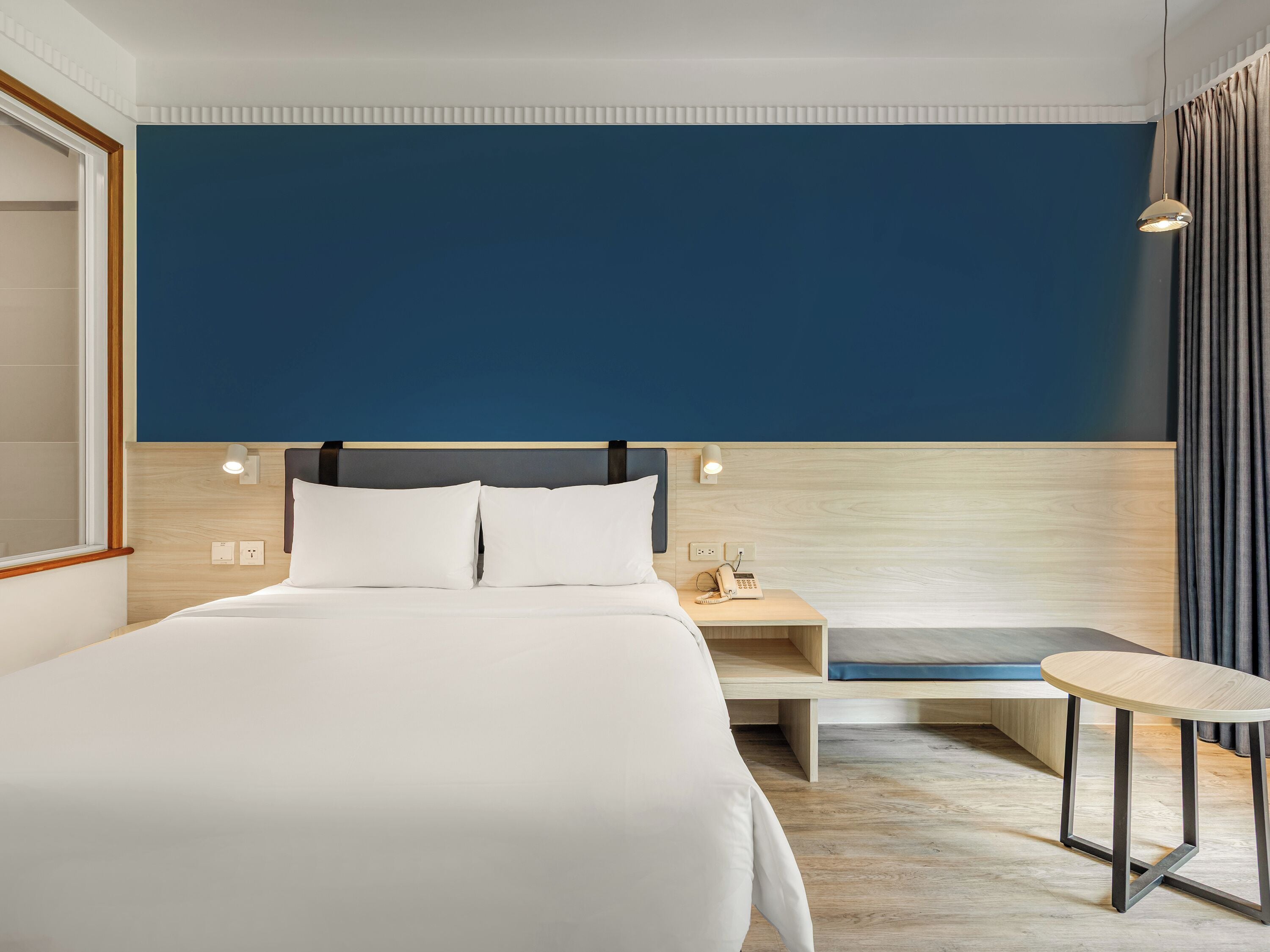 A hotel room with a large bed, bedside table, and a small round table.