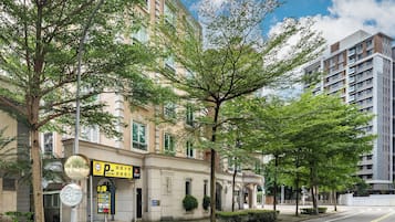 A street view with a building that has a parking sign, a tree-lined sidewalk, and a clear sky.
